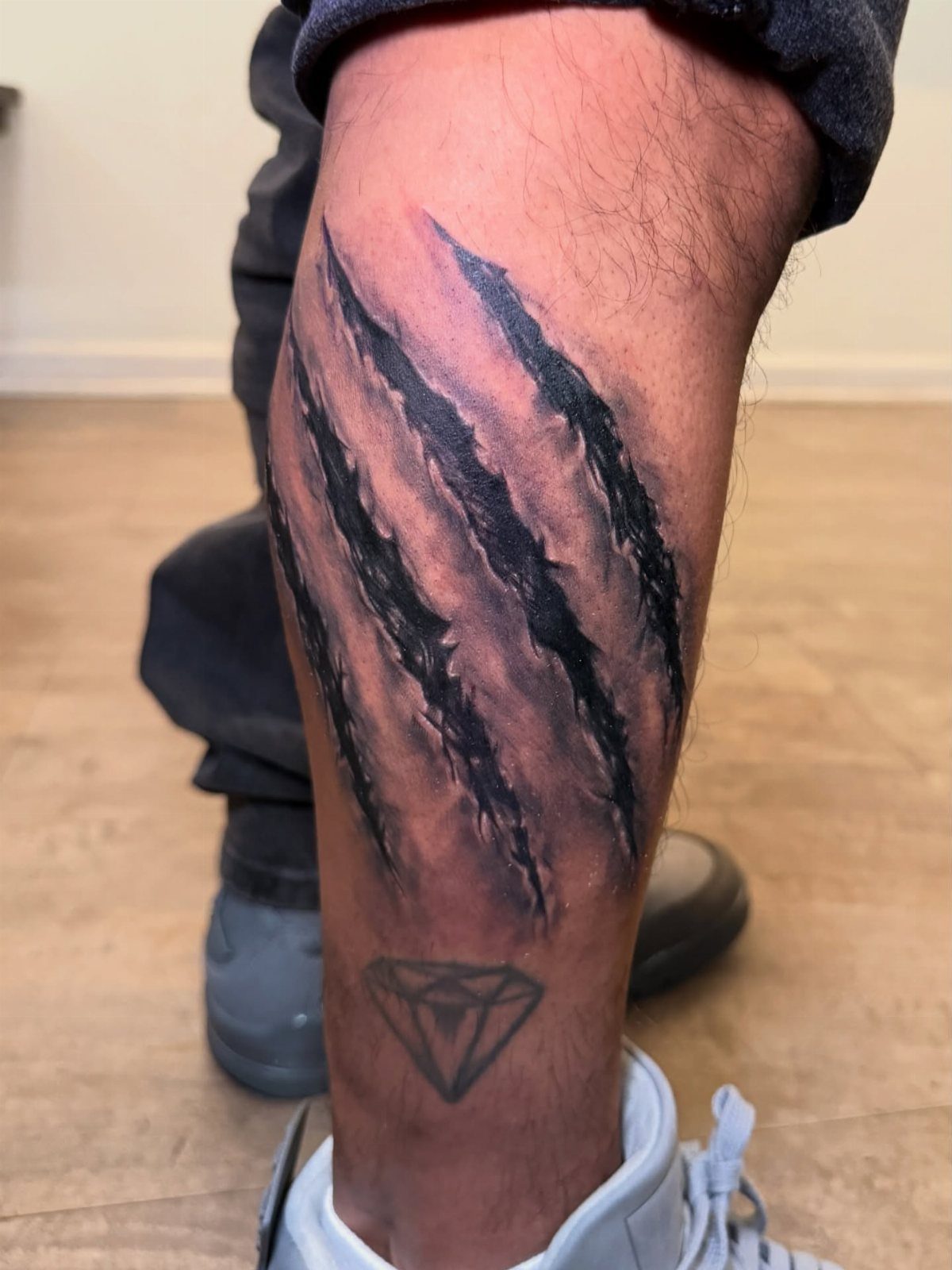 Bear claw mark tattoo and diamond tattoo on a person's lower leg.