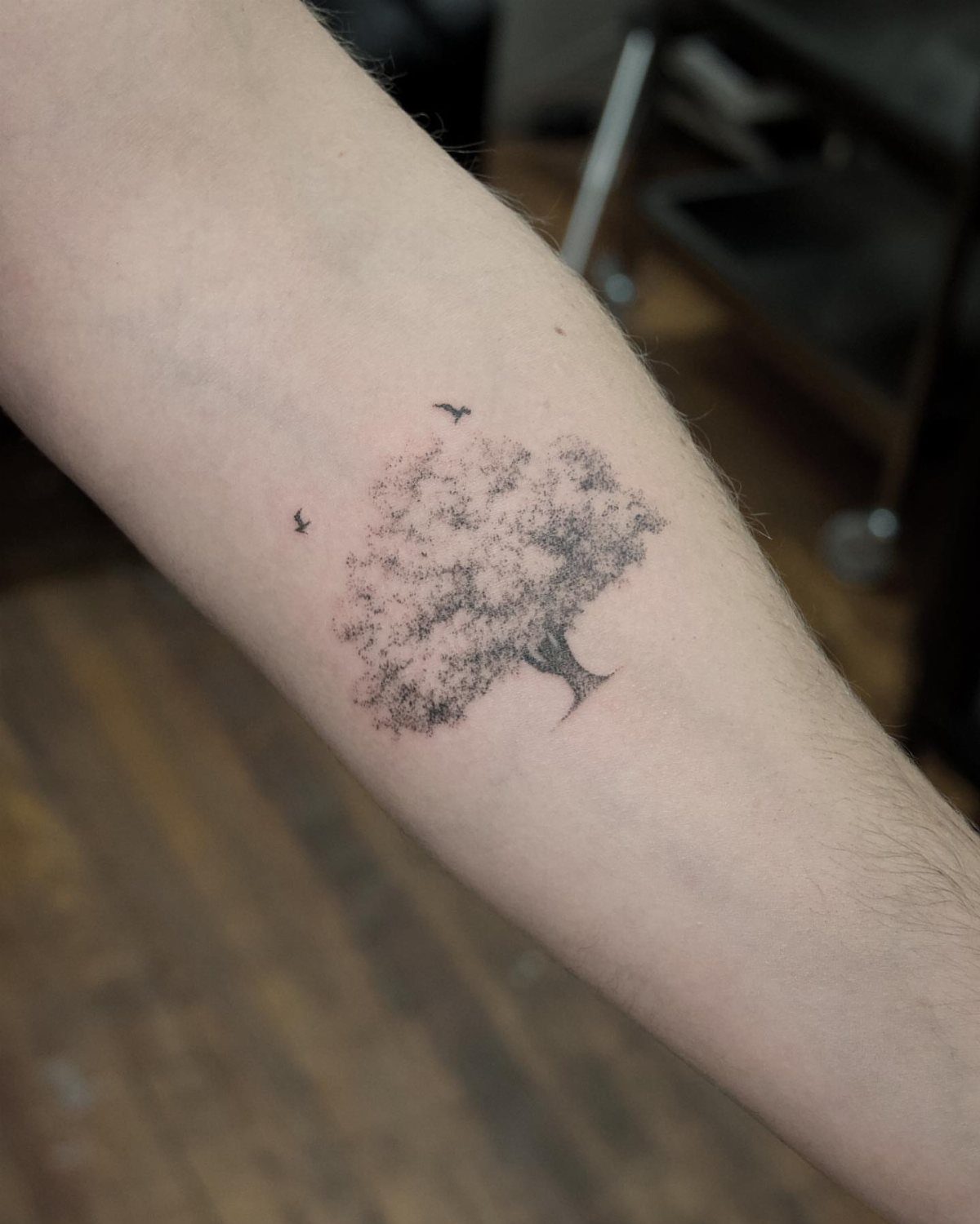 Leafy tree tattoo with two small birds on a person's forearm.