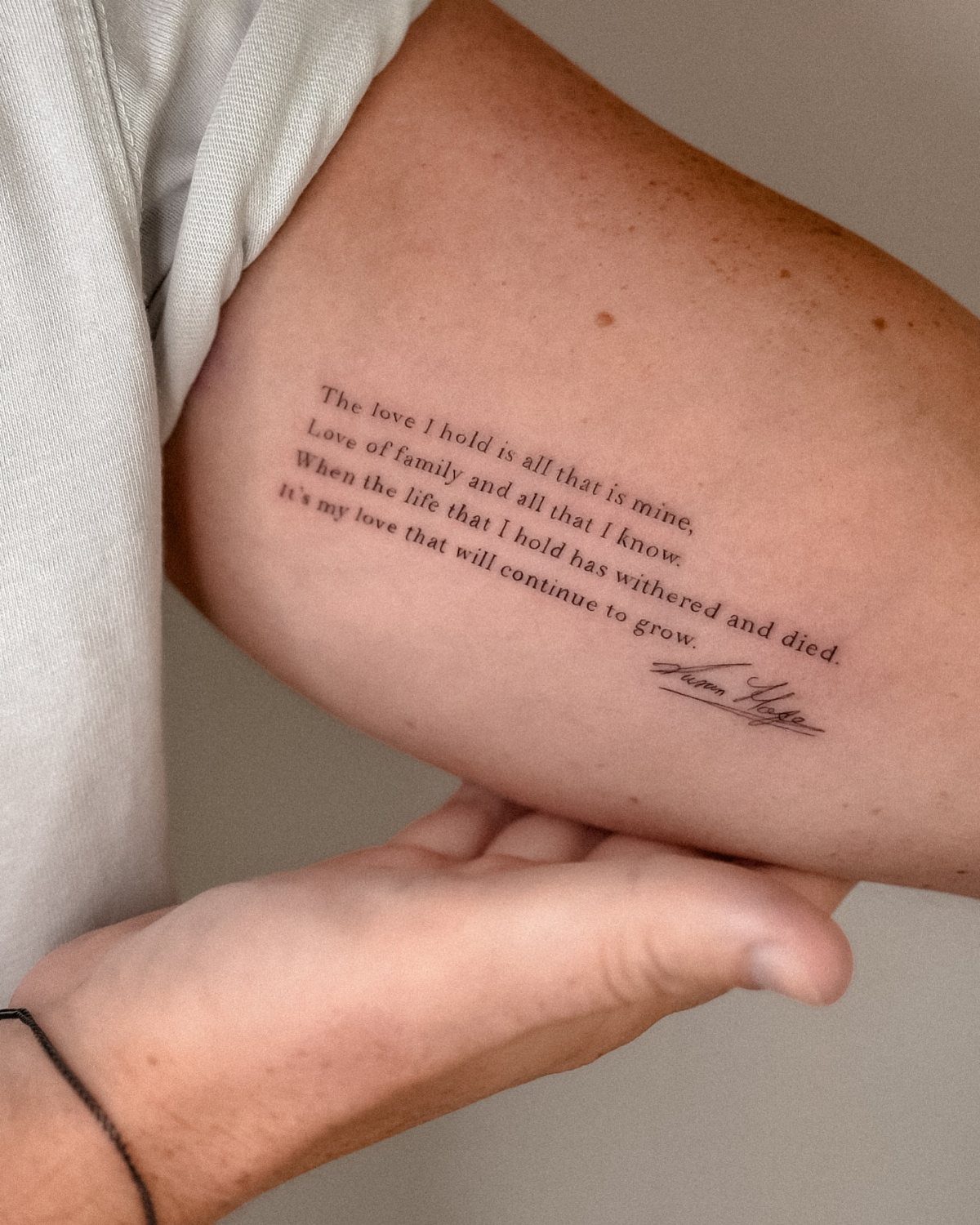 Cursive quote tattoo with thin black lines on a person's upper arm.
