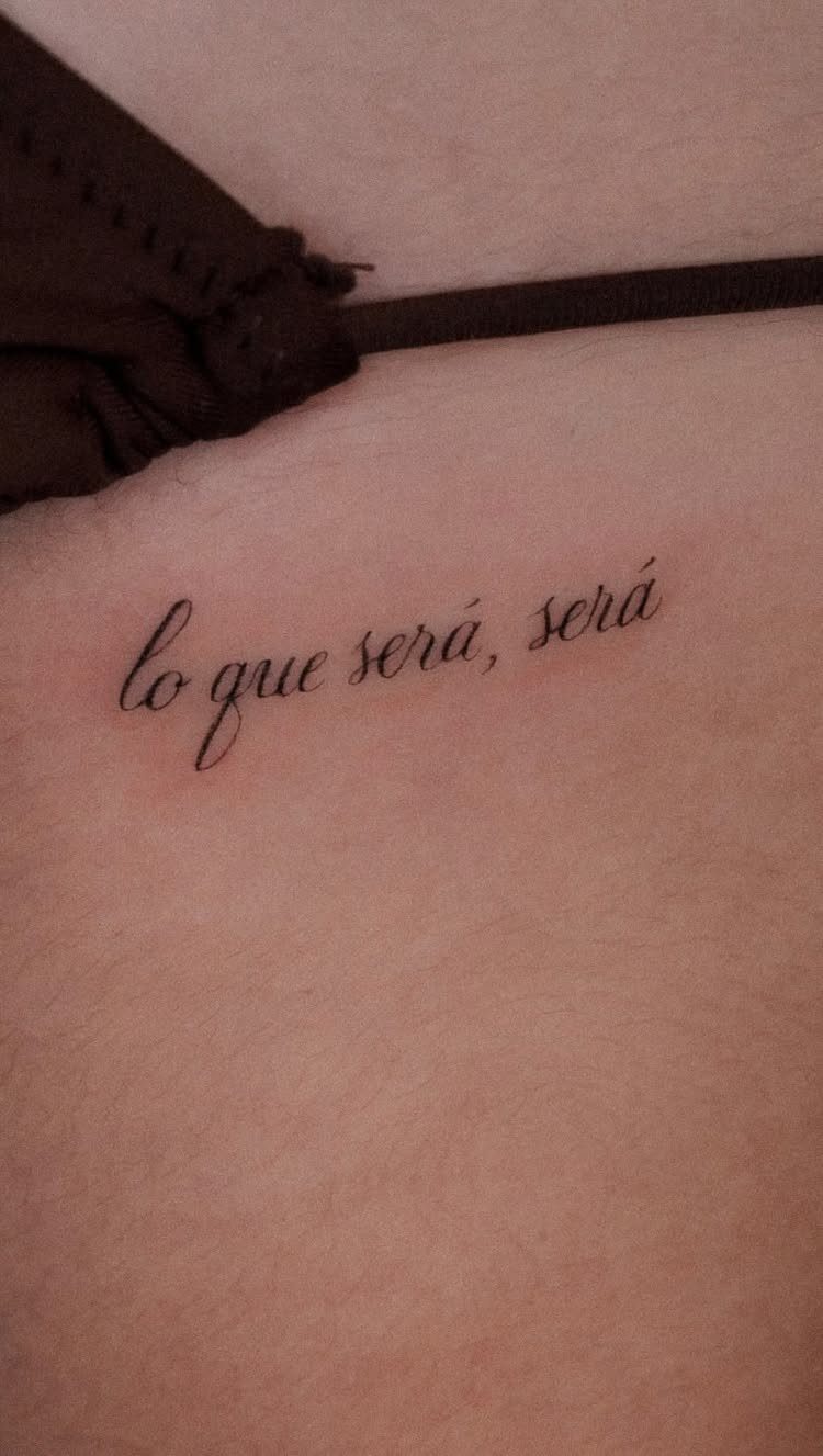 Cursive script tattoo on skin reading lo que será, será in black ink