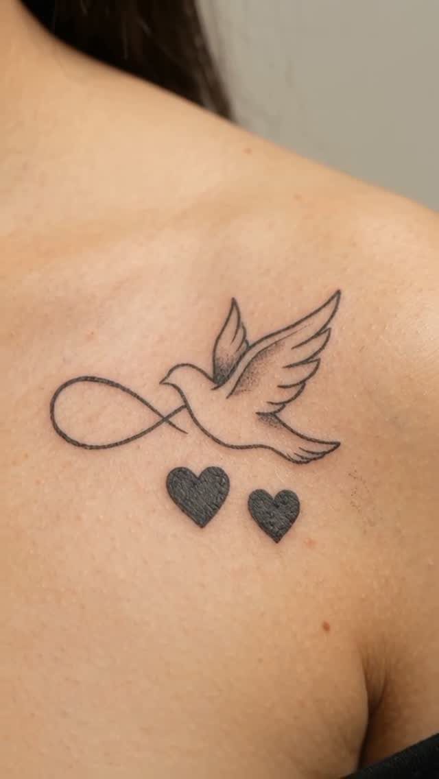 Dove tattoo with an infinity symbol and two hearts on a shoulder