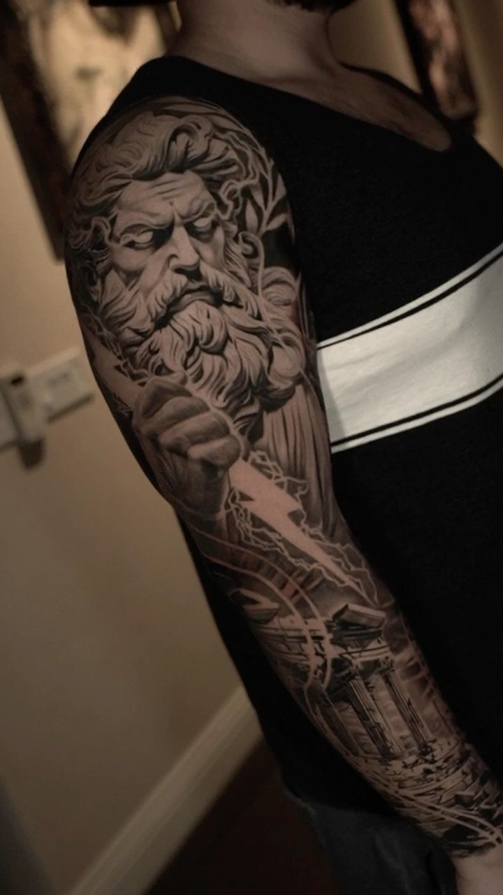 Detailed black and grey tattoo of Zeus with a lightning bolt on an arm.