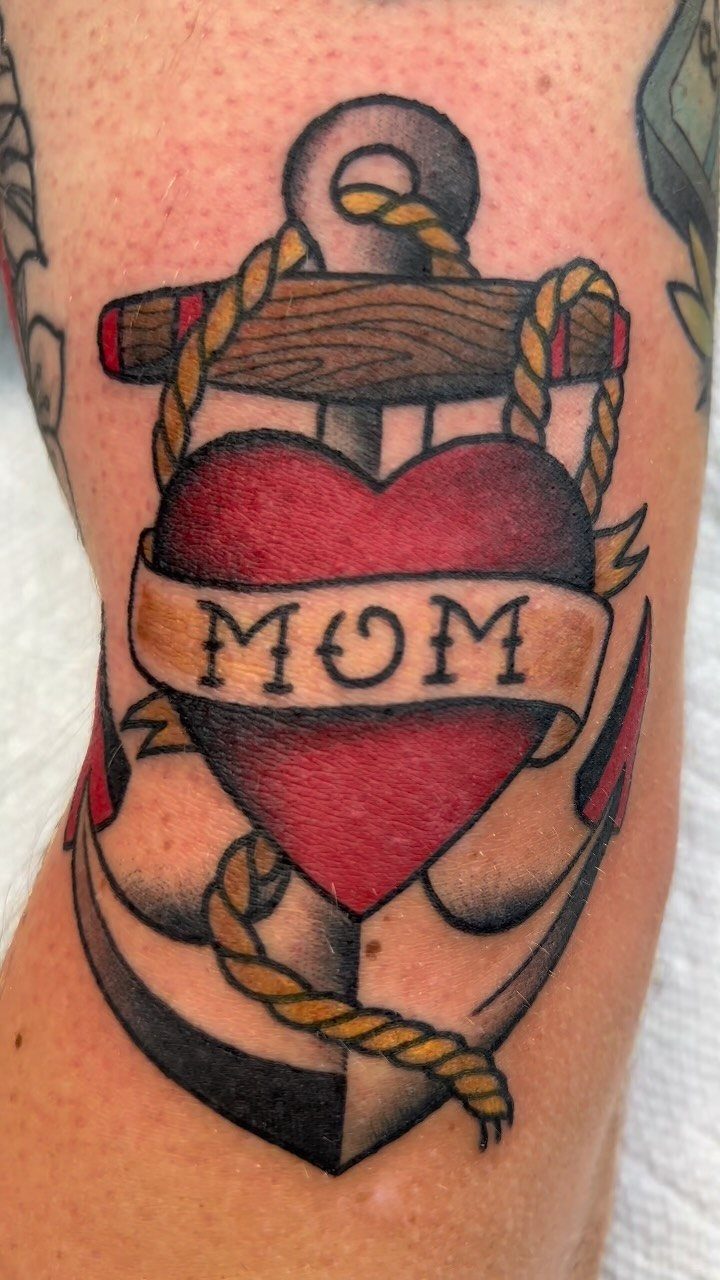 Anchor tattoo with a red heart and a banner reading MOM on skin