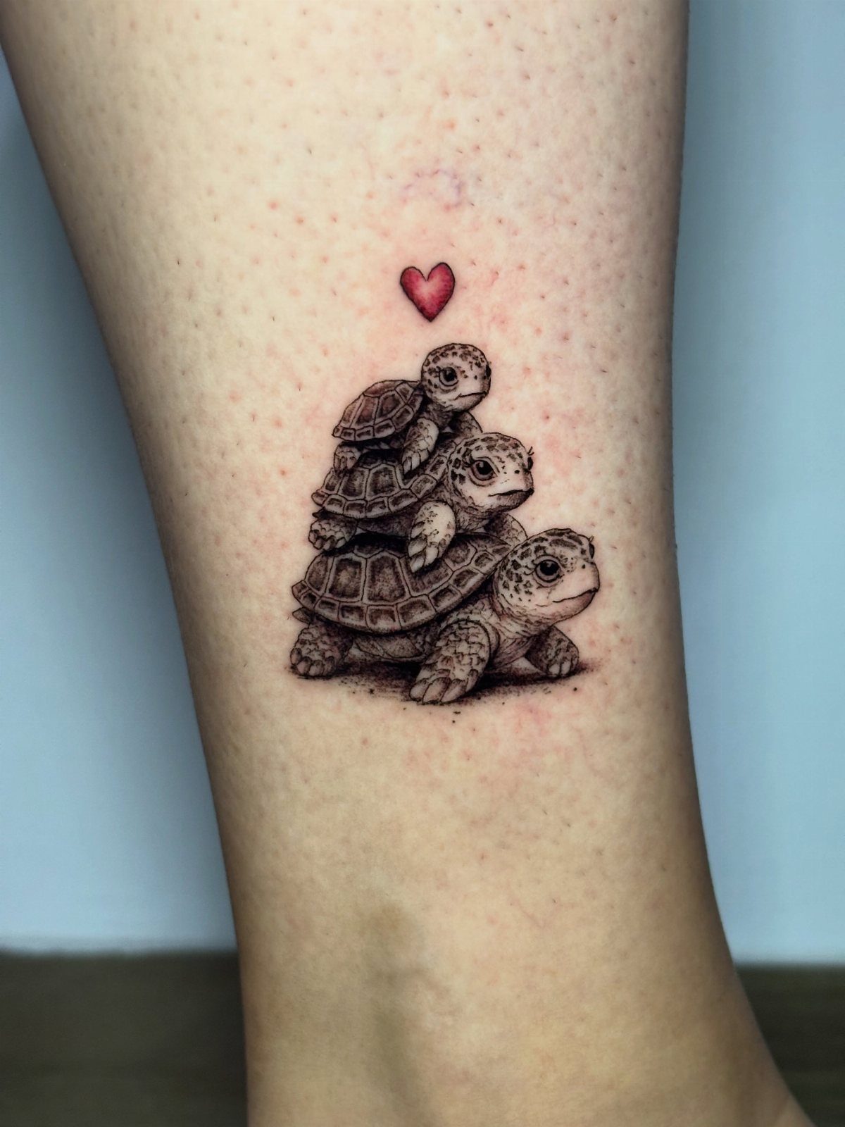 Tattoo of three stacked turtles with a small red heart on an ankle.