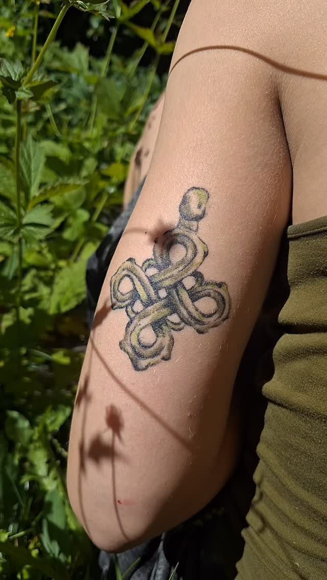 Celtic knot tattoo on a person's upper arm with green foliage background