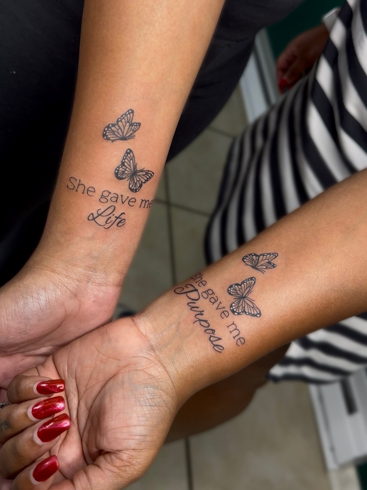 Matching wrist tattoos with butterflies and text about life and purpose.