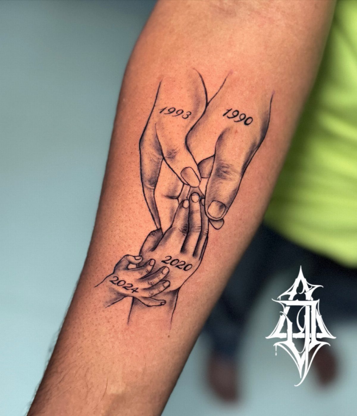 Forearm tattoo of four interlocking hands of different ages with birth years.