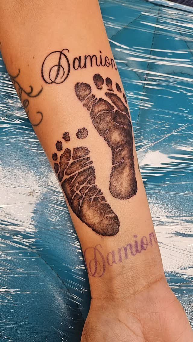 Baby footprint tattoos with the name Damion on a person's forearm