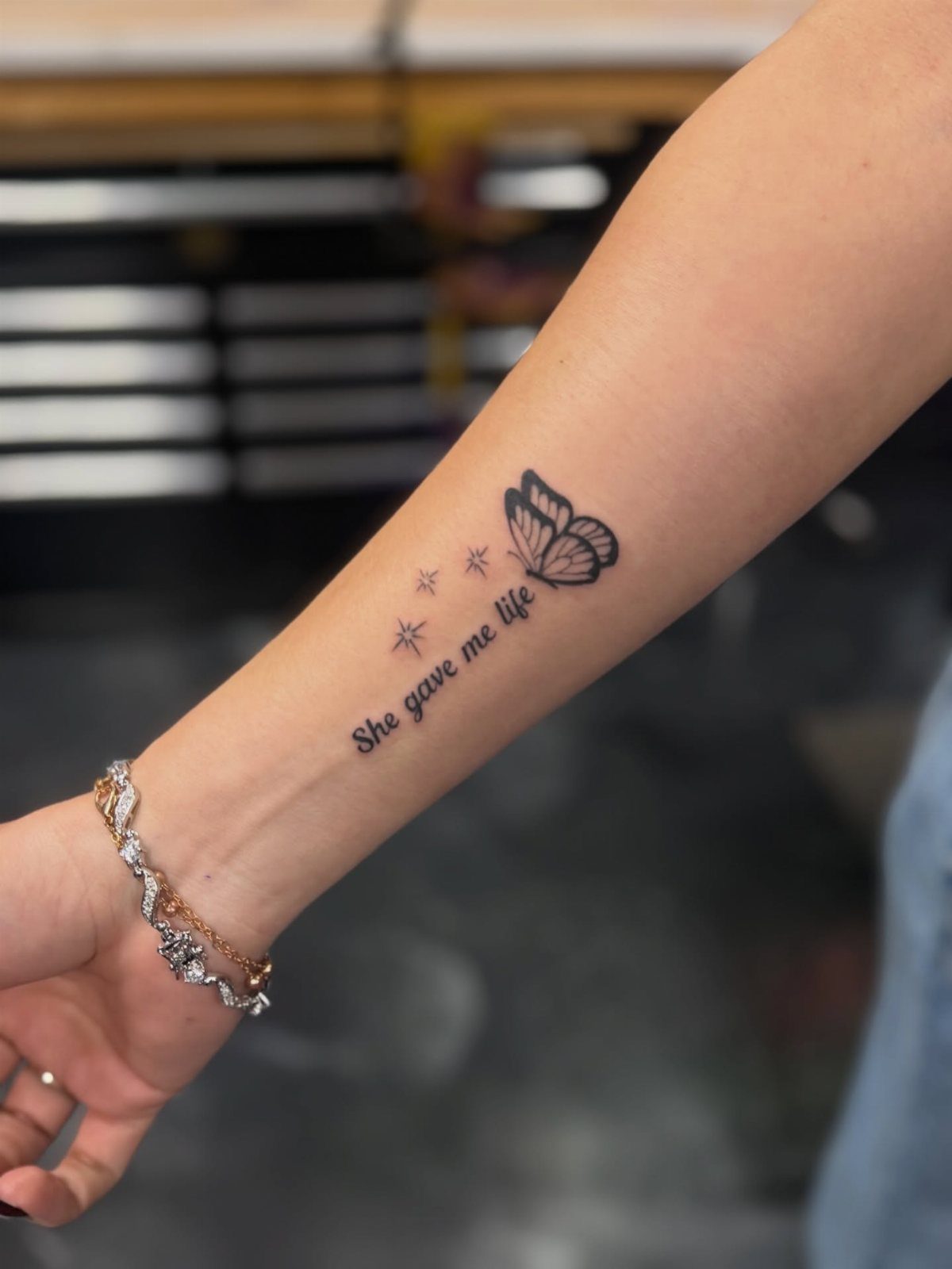 Forearm tattoo with the text She gave me life, stars, and a butterfly.