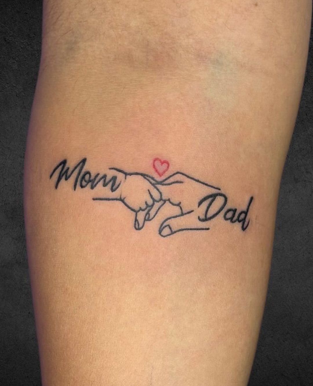 Tattoo on skin showing 'Mom' and 'Dad' with hands and a red heart.