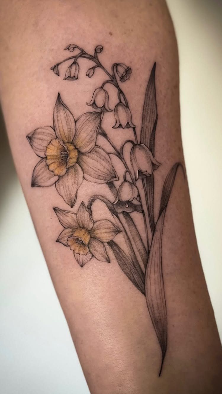 Floral tattoo on an arm featuring daffodils and lily of the valley flowers.