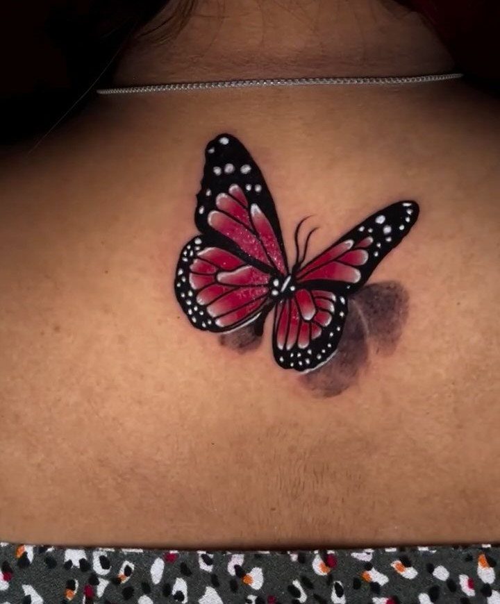 Red and black butterfly tattoo with 3D shadow on a person's chest