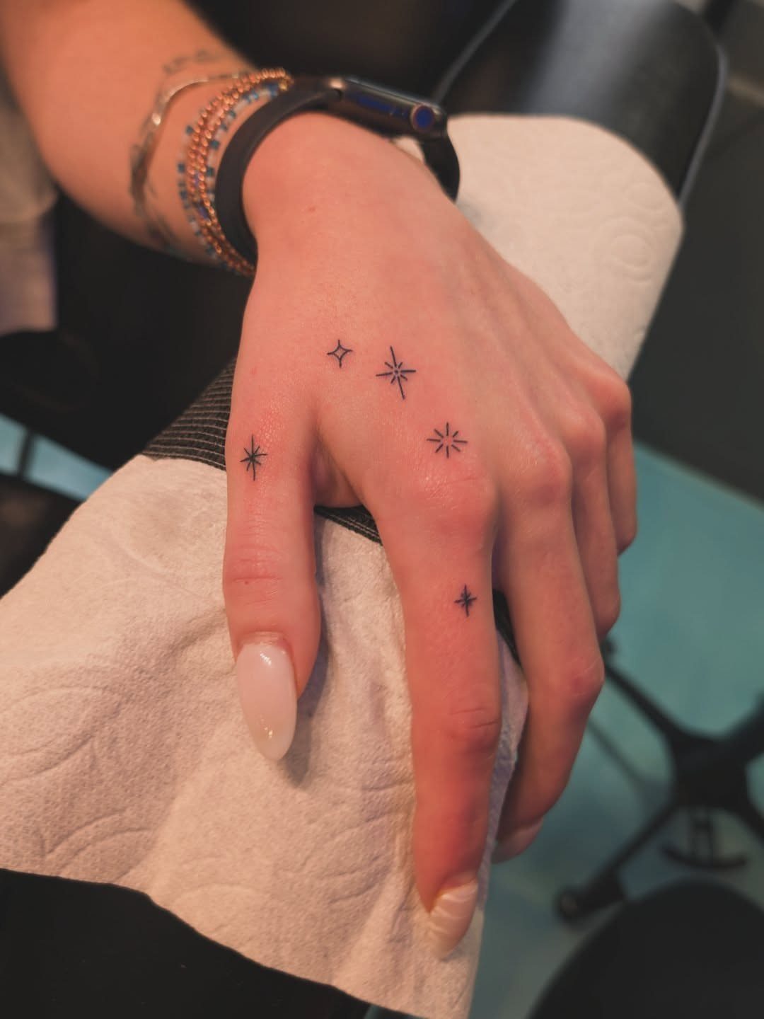 Hand with small black star tattoos on the fingers and back of hand.