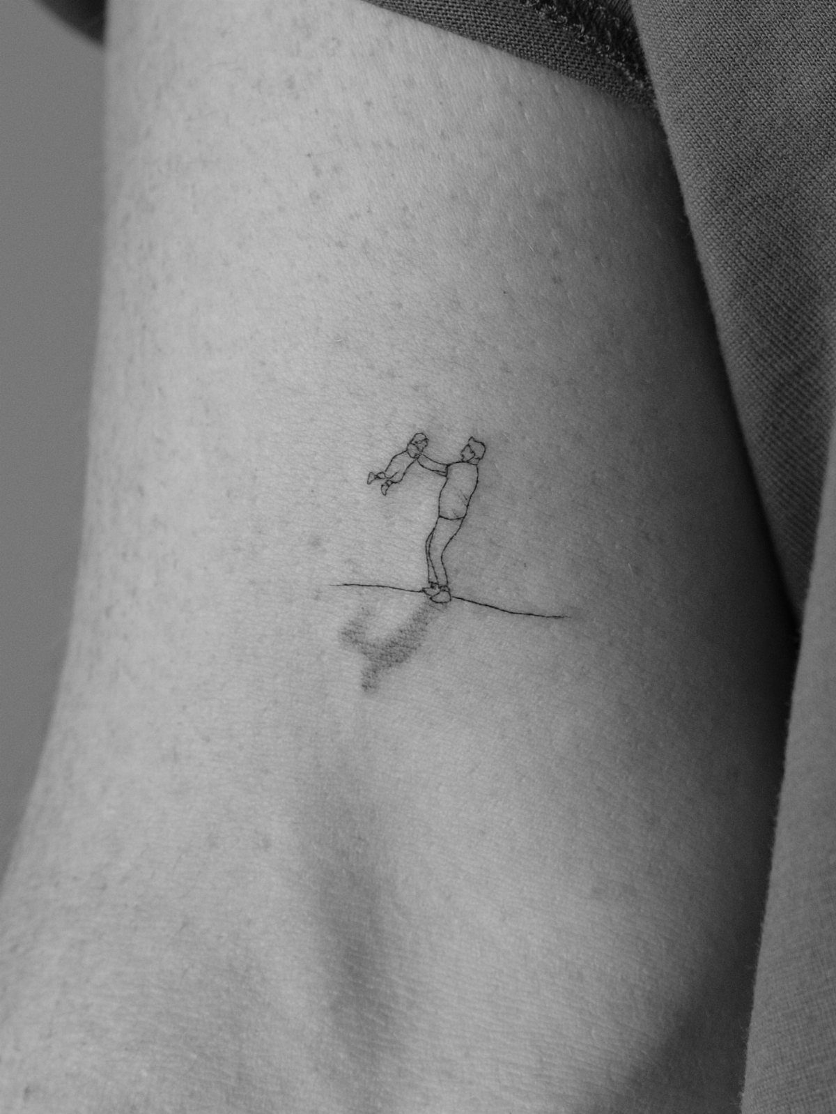 Minimalist line-art tattoo of a father lifting a baby on an arm