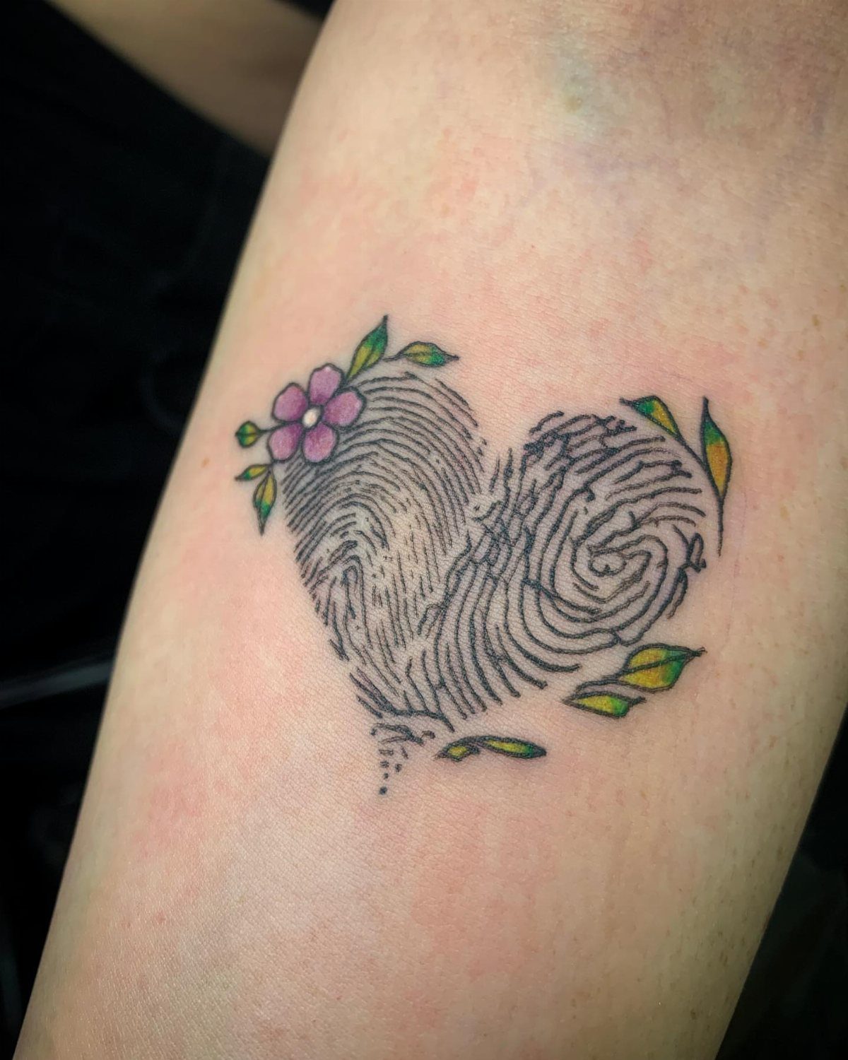 Fingerprint heart tattoo with a small purple flower and green leaves on skin