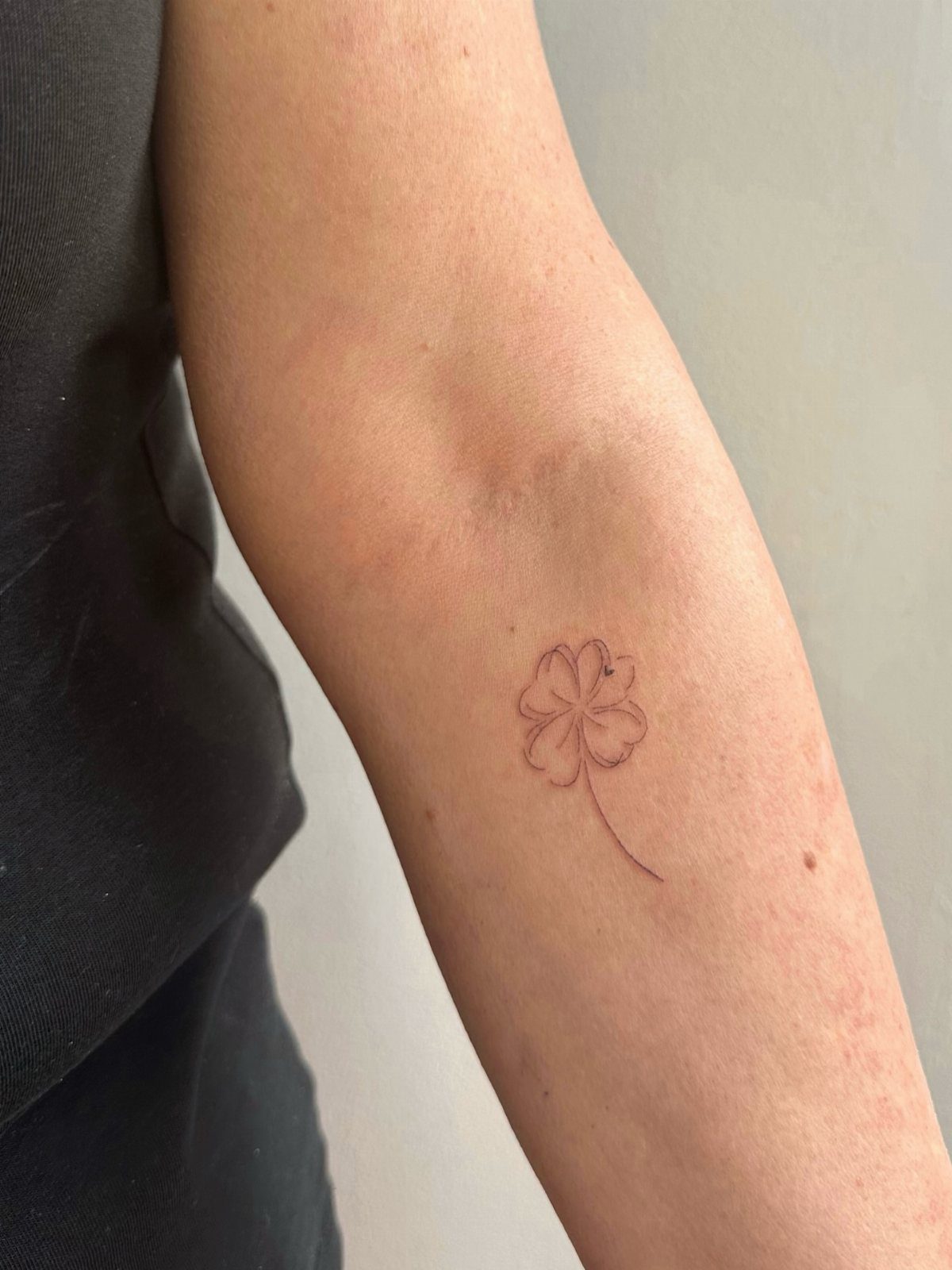 Small red four-leaf clover tattoo on a person's inner forearm.