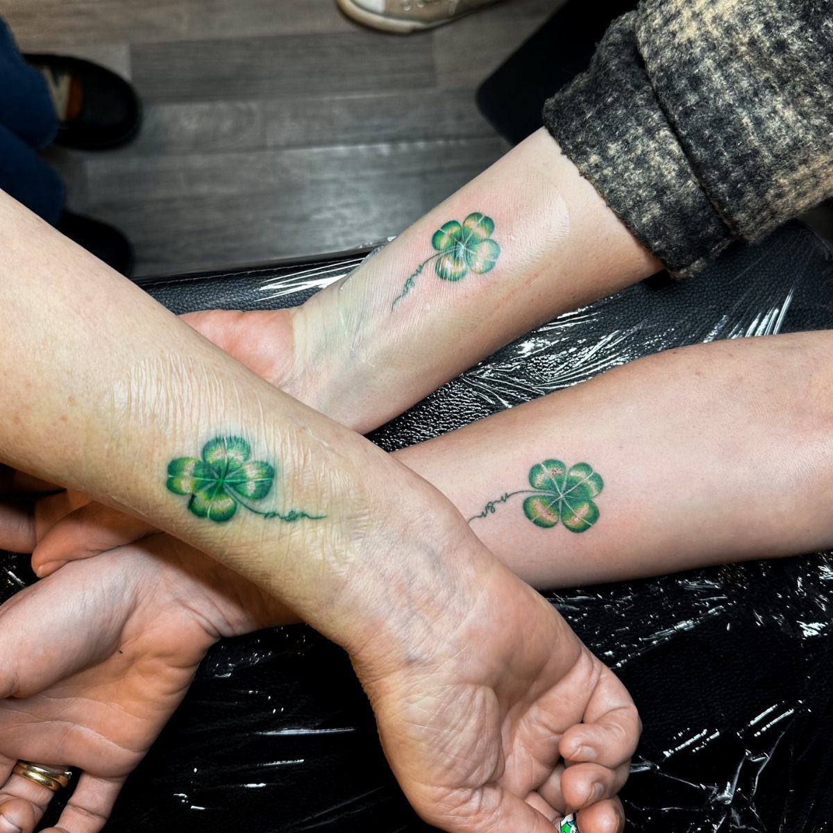 Three matching green four-leaf clover tattoos on the wrists of three different people.