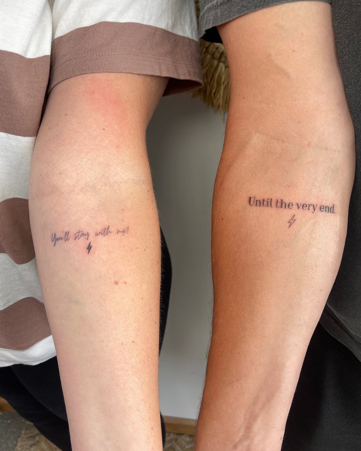 Two forearms with matching script tattoos and lightning bolts about staying together.