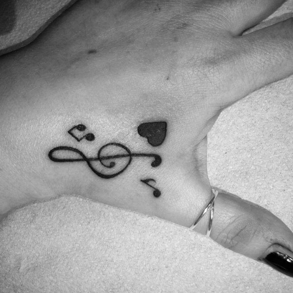 Tattoo of a treble clef, musical notes, and a heart on a wrist.