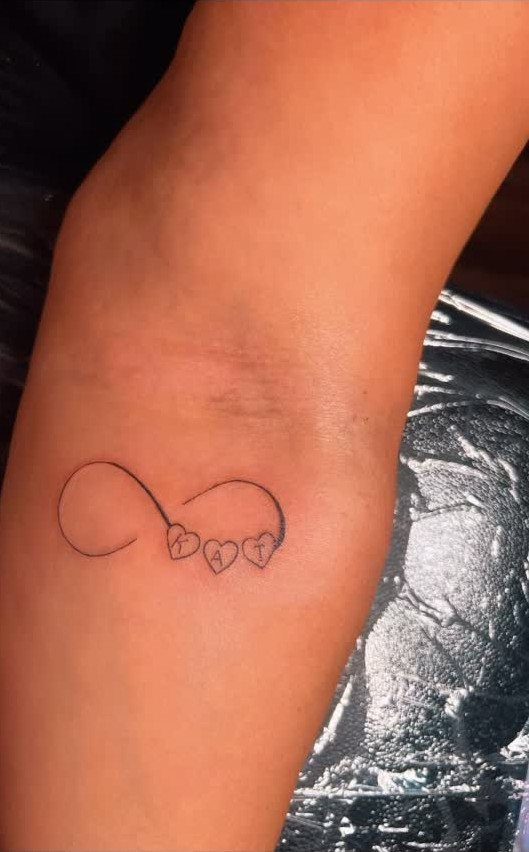 Infinity symbol tattoo with two small hearts on a person's inner forearm.