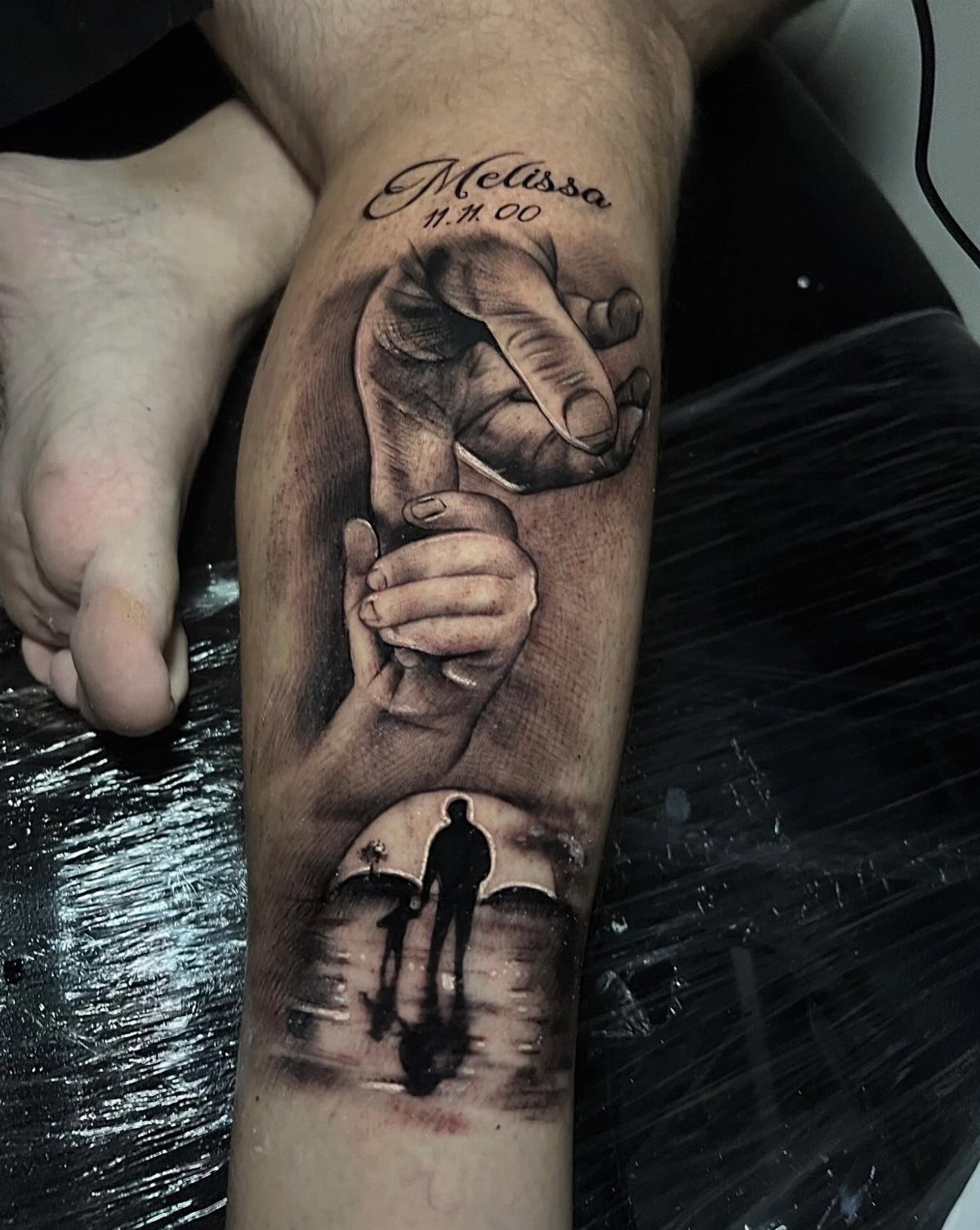 Realism tattoo of a large hand holding a small hand and family silhouettes.