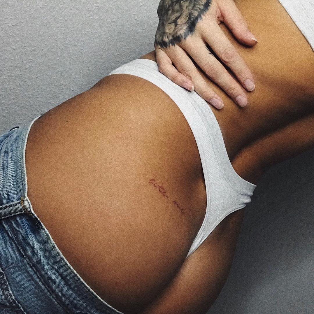 Cursive word tattoo on a woman's hip wearing white underwear and denim.