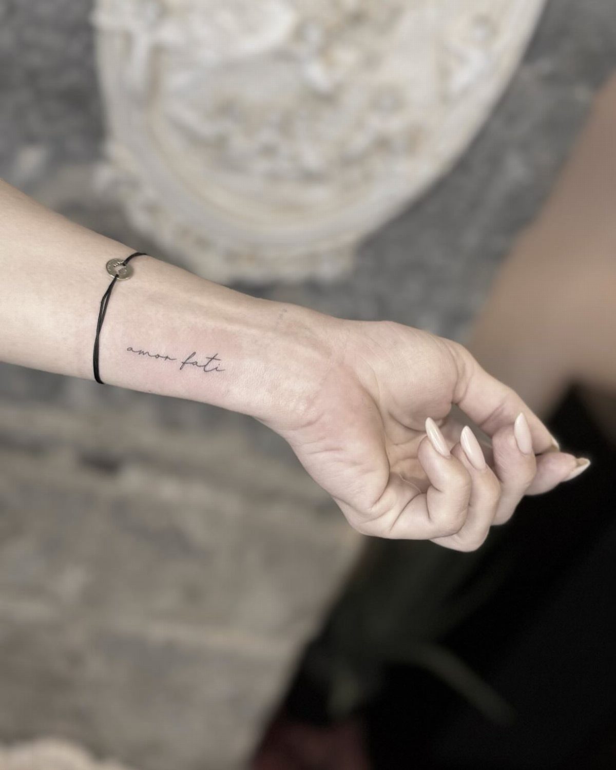 Wrist with a cursive amor fati tattoo and long white manicured nails