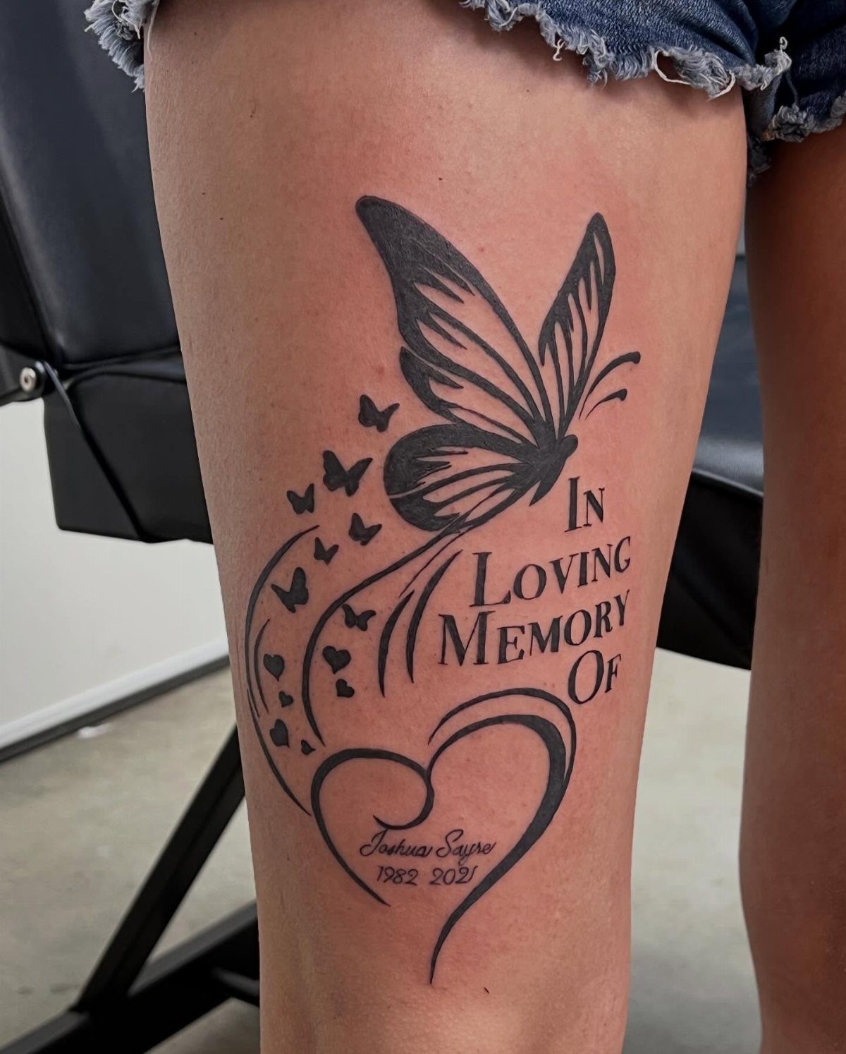 Butterfly and heart memorial tattoo on a thigh with name and dates.