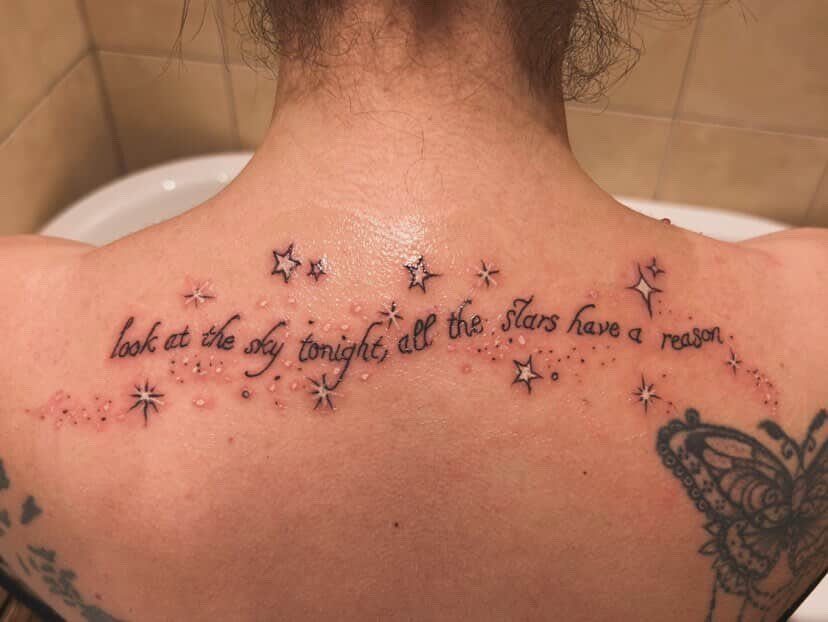 Tattoo on a person's upper back with a quote and small white stars.