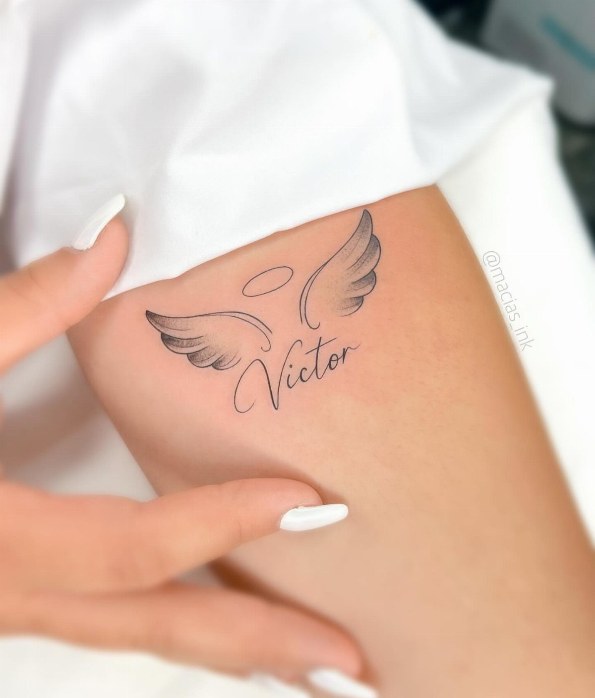 Tattoo of angel wings, a halo, and the name Victor on skin