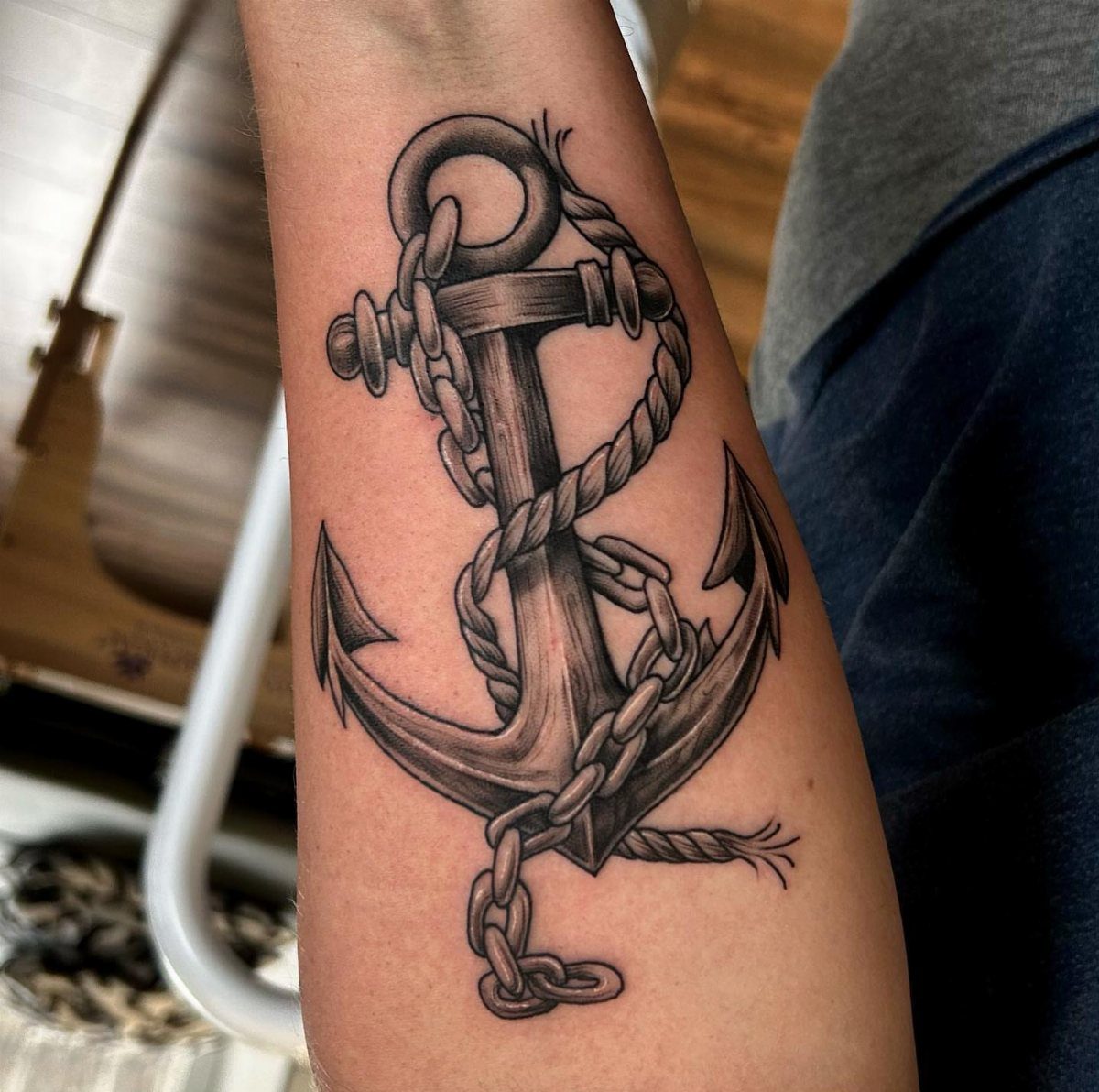 Anchor tattoo with rope and chain on a person's forearm in black and grey.