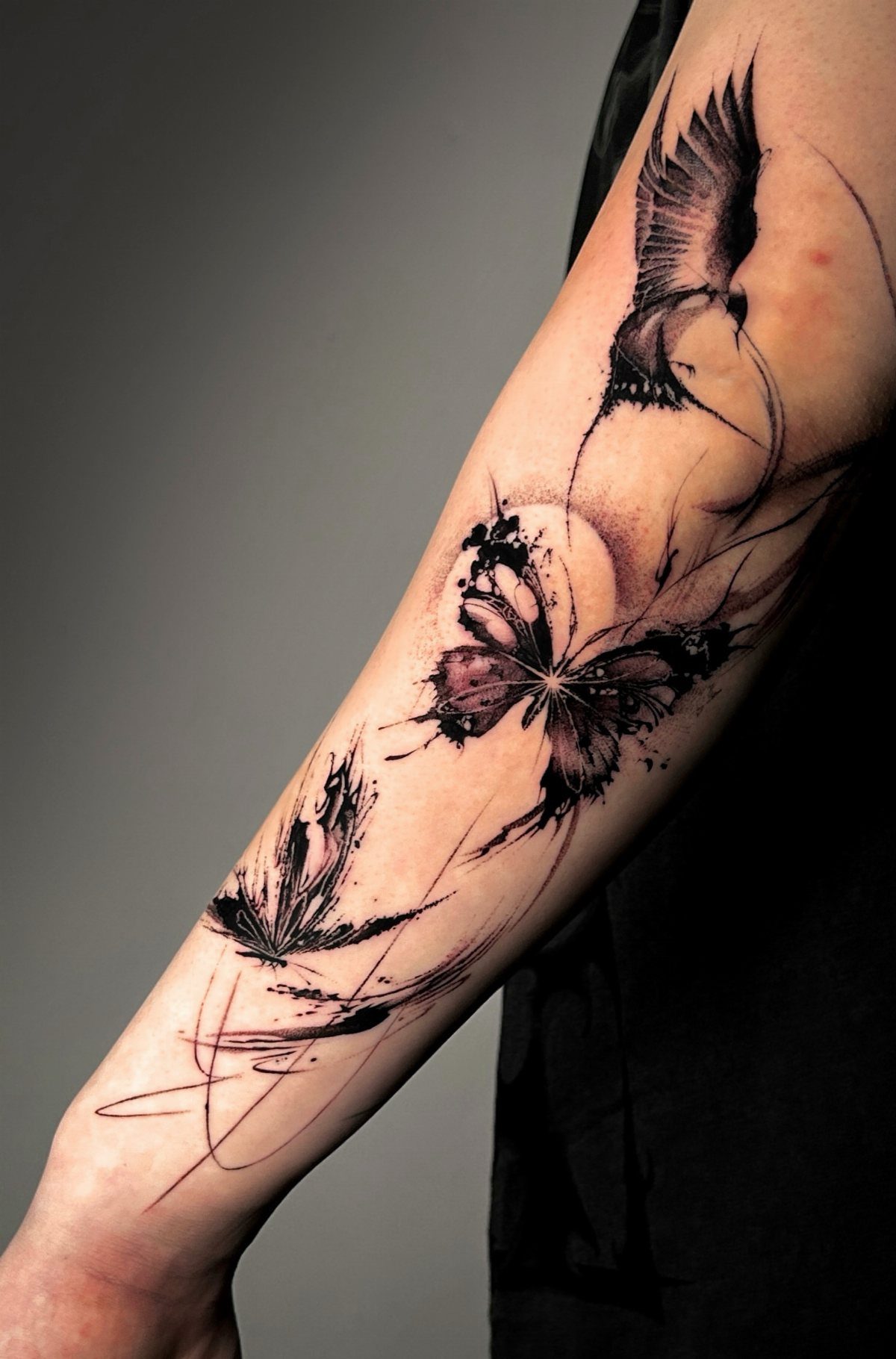 Butterfly tattoo on a forearm with a bird and lotus flower in black ink