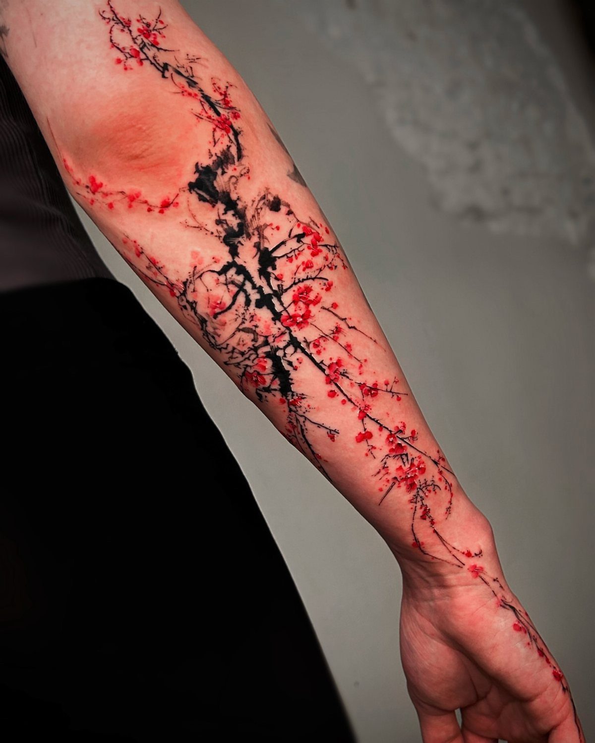 Cherry blossom tattoo with red flowers and black branches on a person's forearm