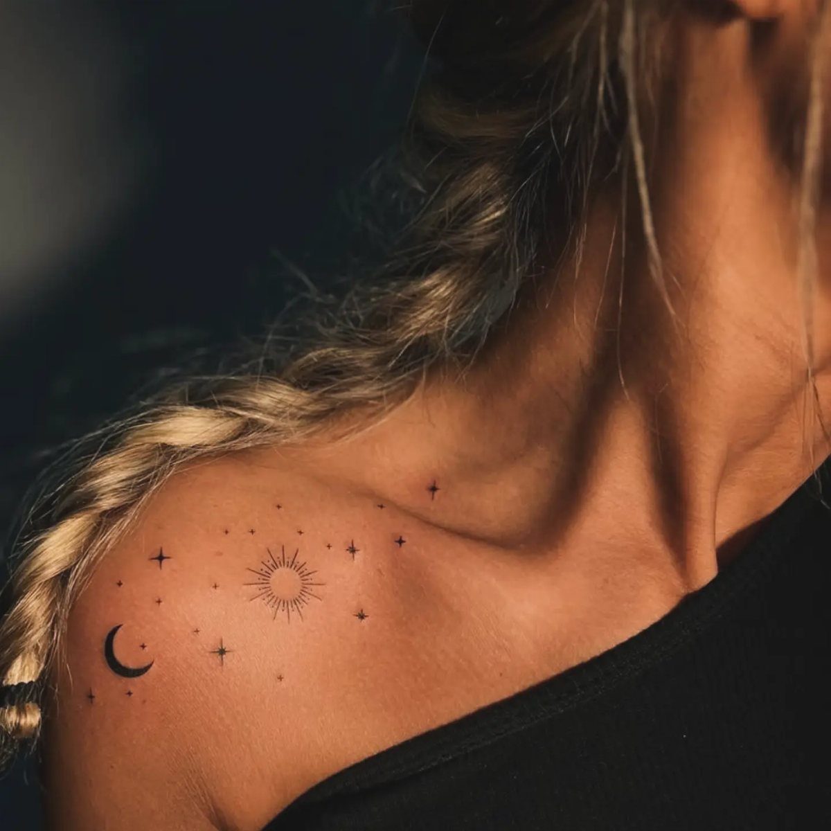 Crescent moon, sun, and stars tattoos on a person's shoulder and collarbone.