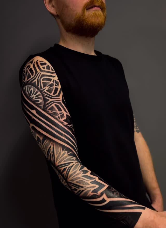 Geometric pattern tattoo on a man's arm with bold black ink designs.