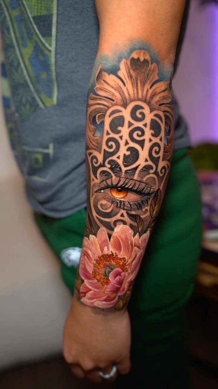 Hamsa hand tattoo with an eye and pink lotus flower on a forearm