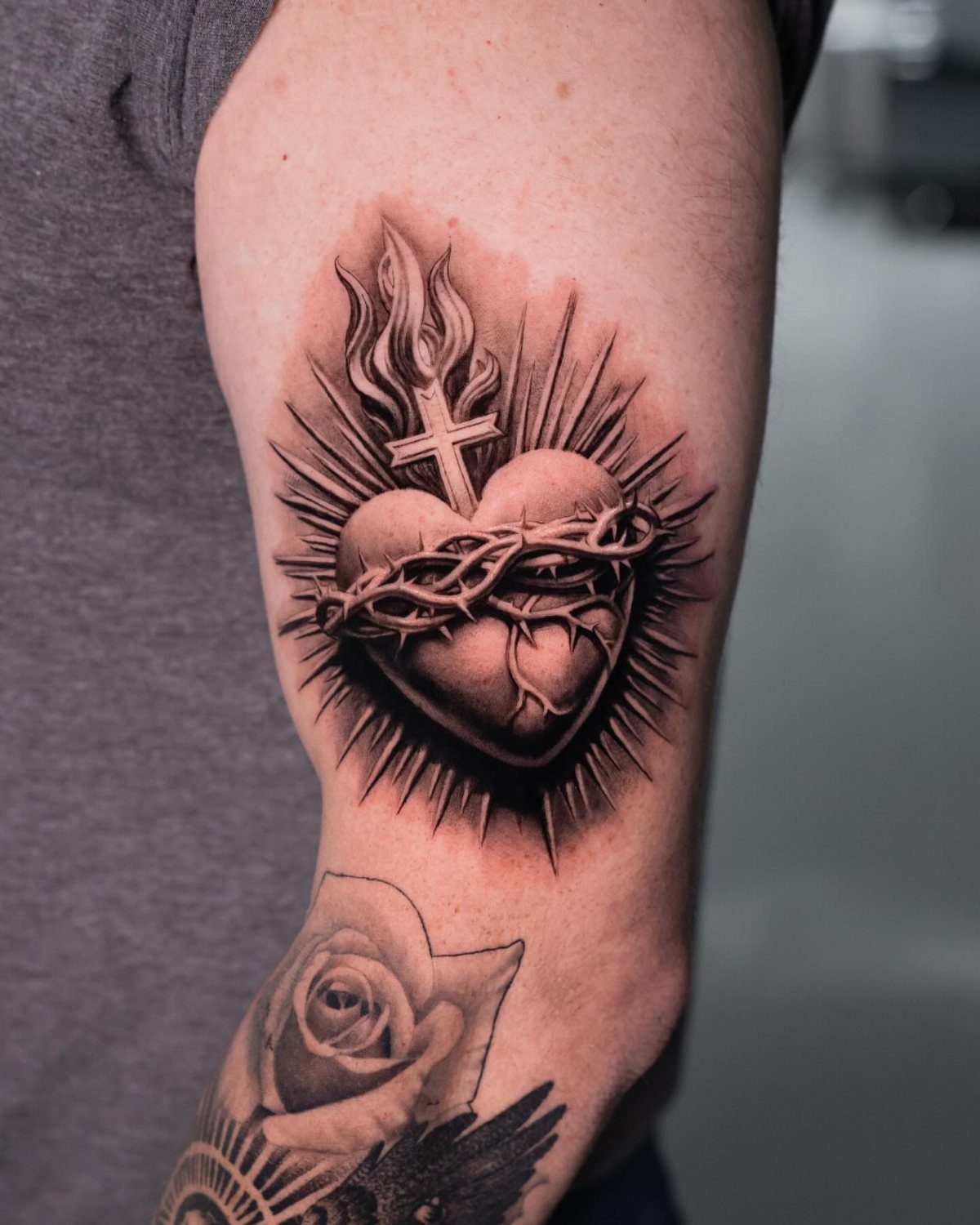 Heart tattoo with crown of thorns, cross, and flames on an upper arm.