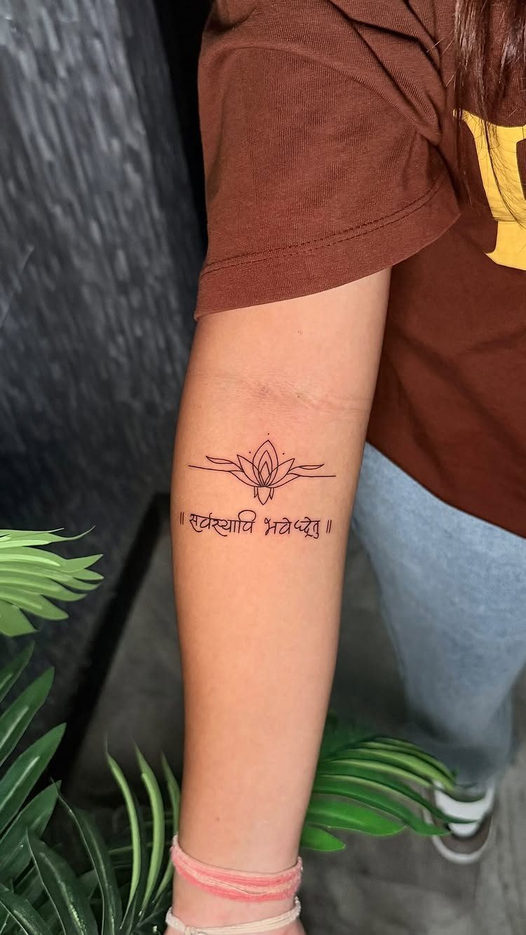 Lotus flower tattoo with script text on a person's inner forearm.