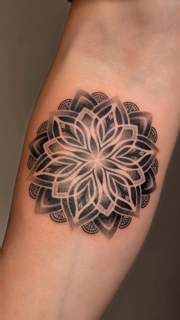 Mandala tattoo with intricate symmetrical geometric patterns on a person's forearm.