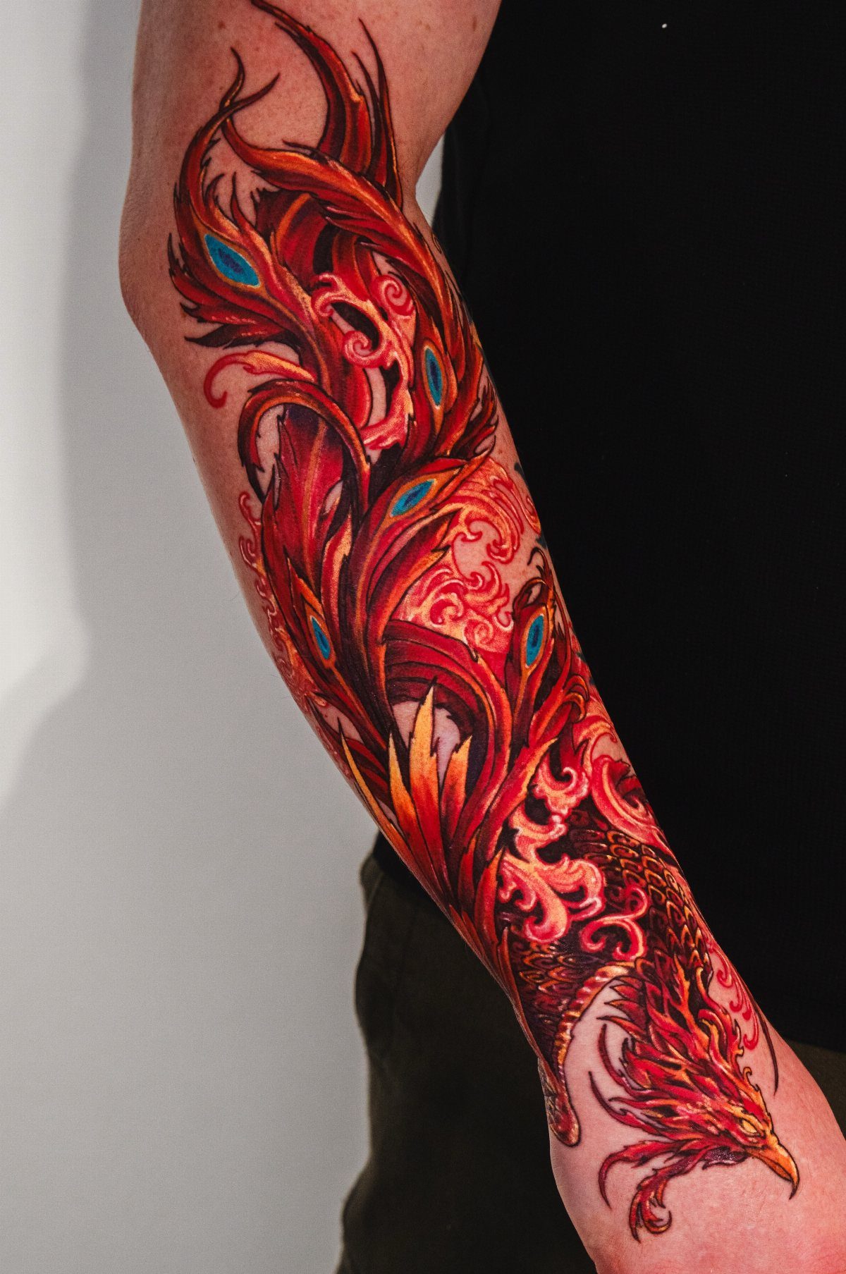 Red and orange phoenix tattoo with blue accents covering a person's forearm