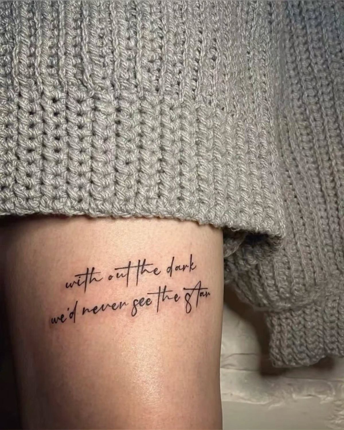 Handwritten quote tattoo on a thigh reading without the dark we'd never see the stars