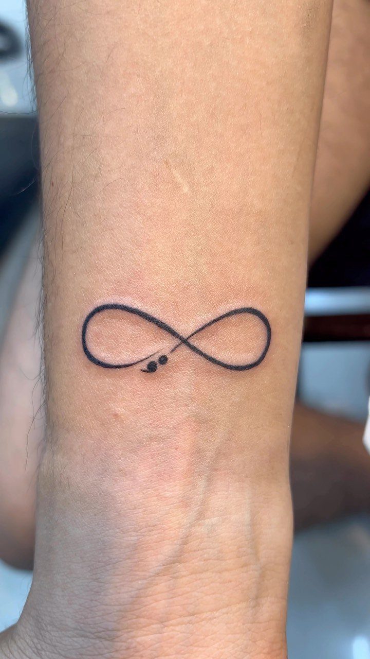 Infinity symbol tattoo with a semicolon on a person's inner wrist