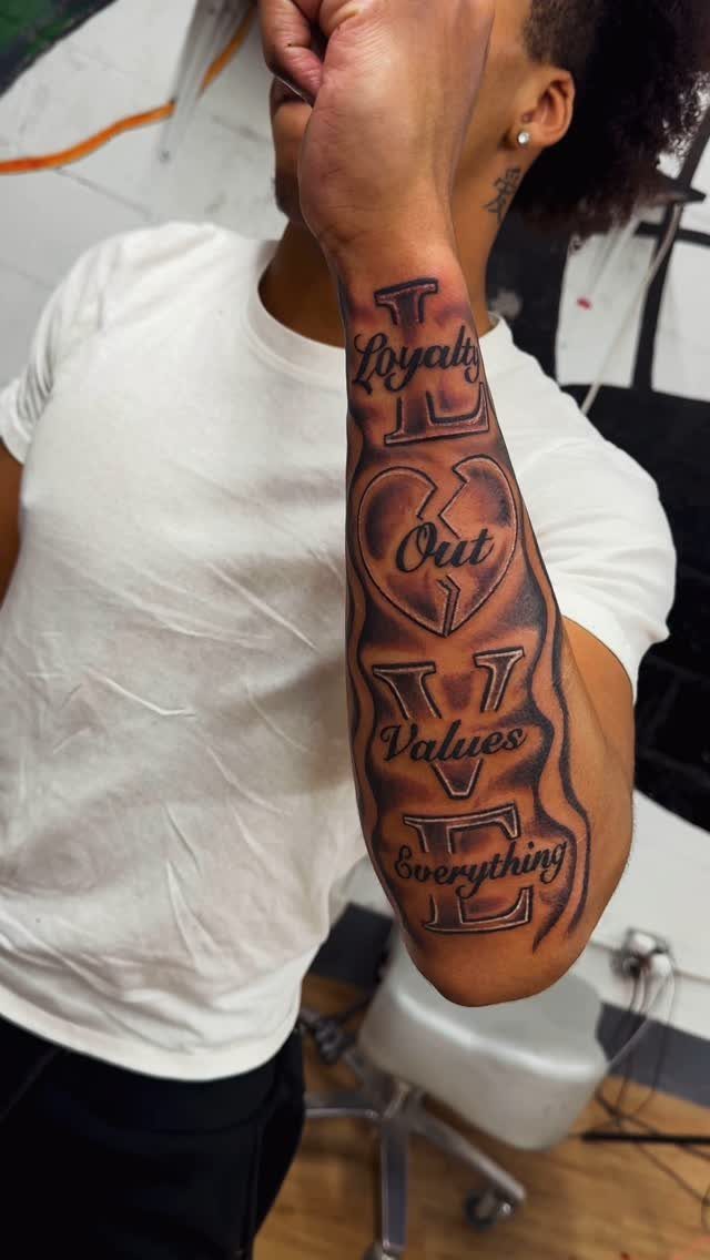 Forearm tattoo spelling LOVE with words Loyalty, Out, Values, Everything and broken heart.