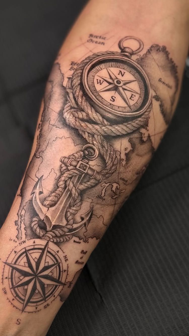 Detailed black and grey tattoo of compasses and an anchor on a forearm.