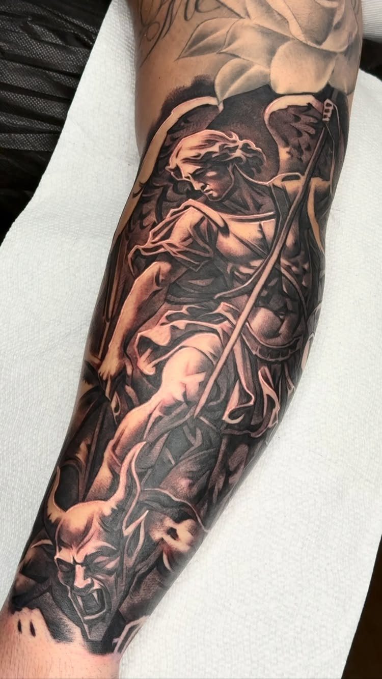 Detailed black and grey tattoo of an angel defeating a horned demon on forearm