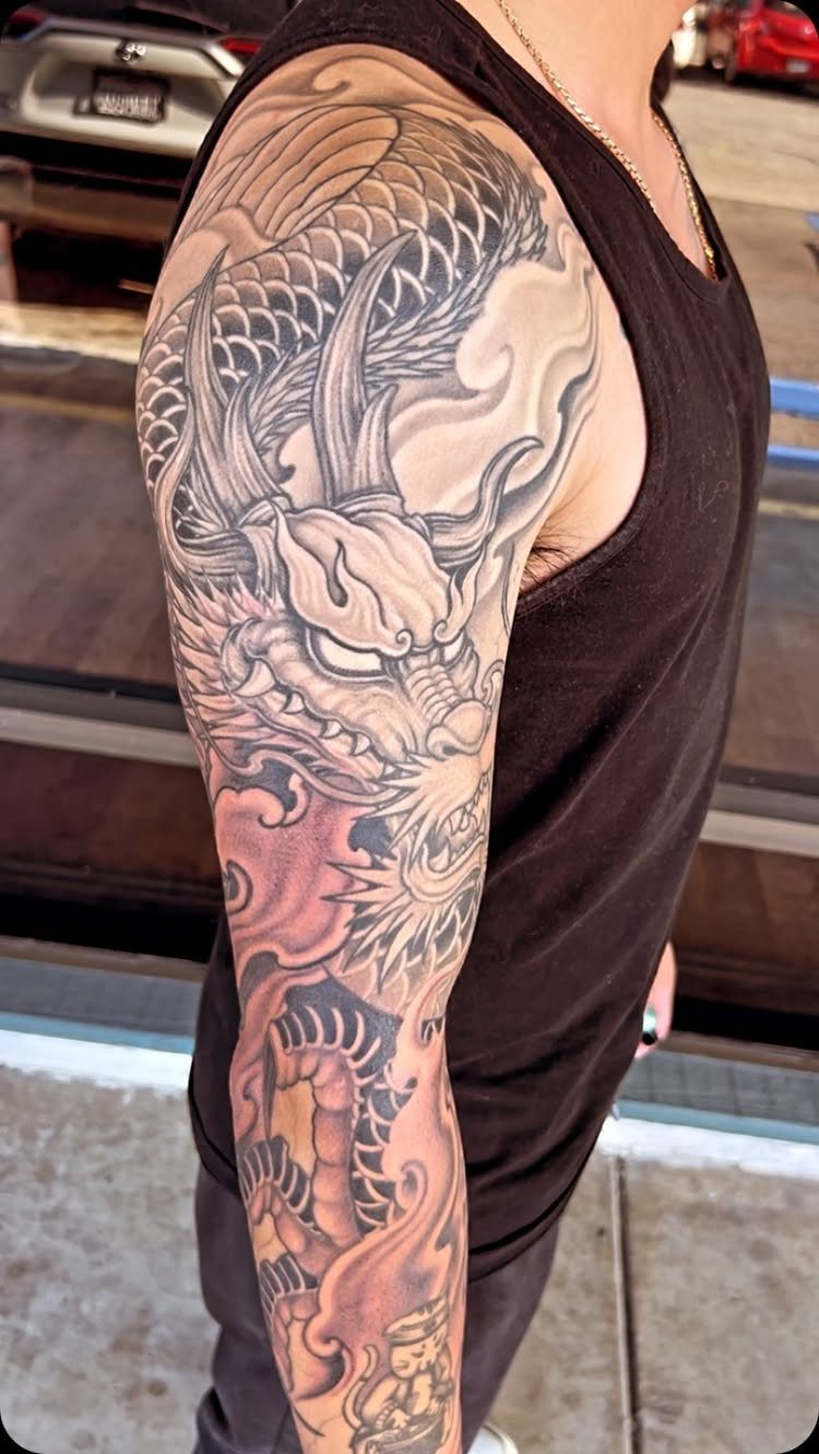 Detailed black and grey dragon tattoo covering a man's shoulder and upper arm.