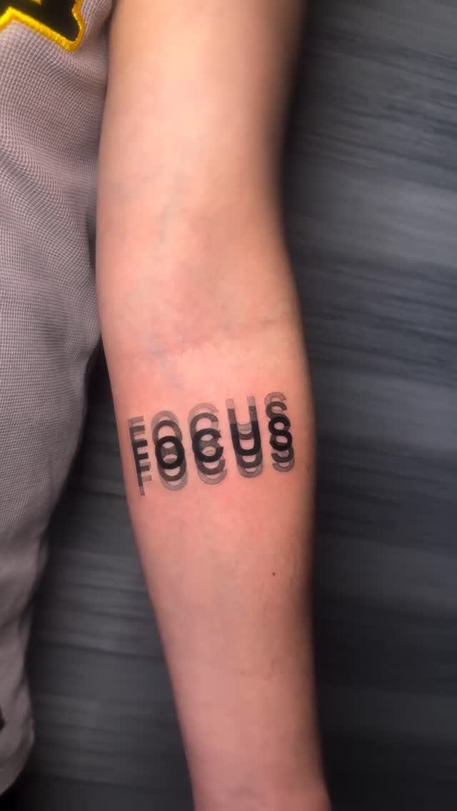 Forearm tattoo of the word FOCUS with a black glitch effect design.