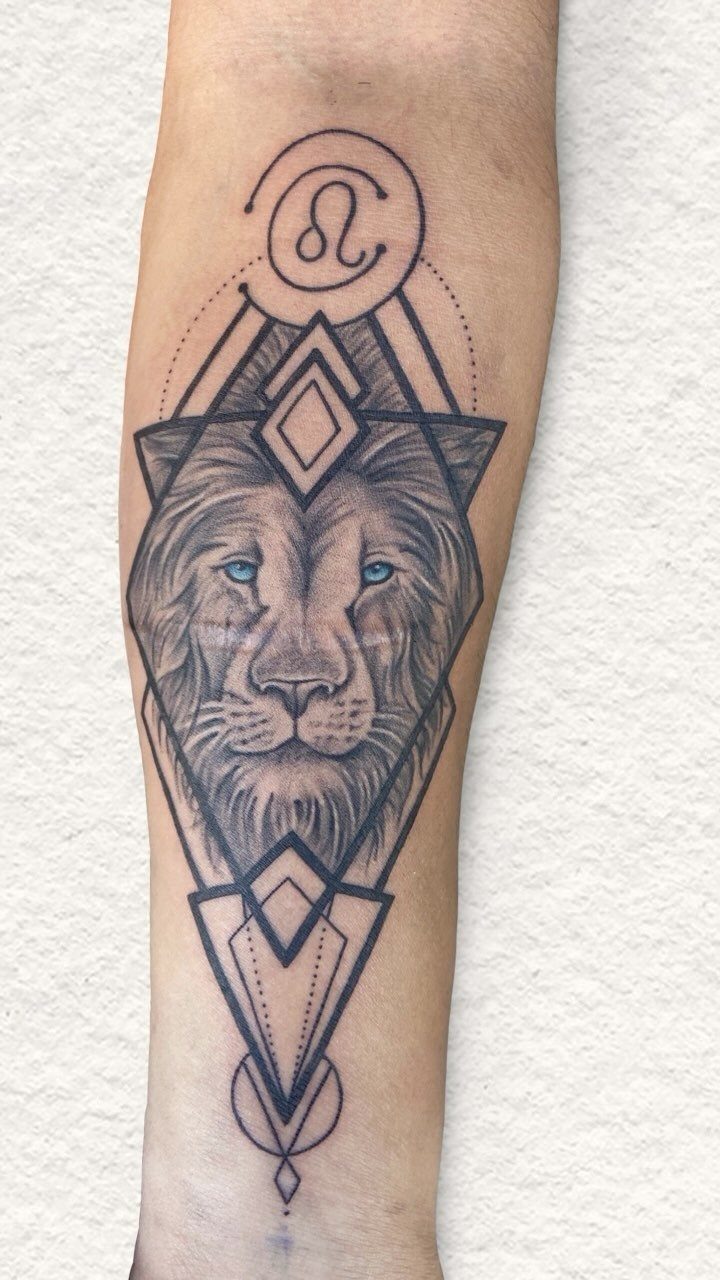 Lion tattoo with blue eyes and geometric patterns on a man's forearm