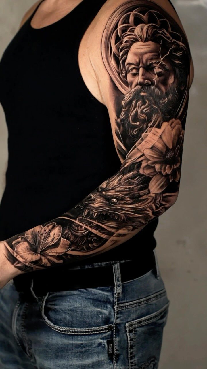 Detailed black and grey tattoo of a bearded man and flowers on a man's arm
