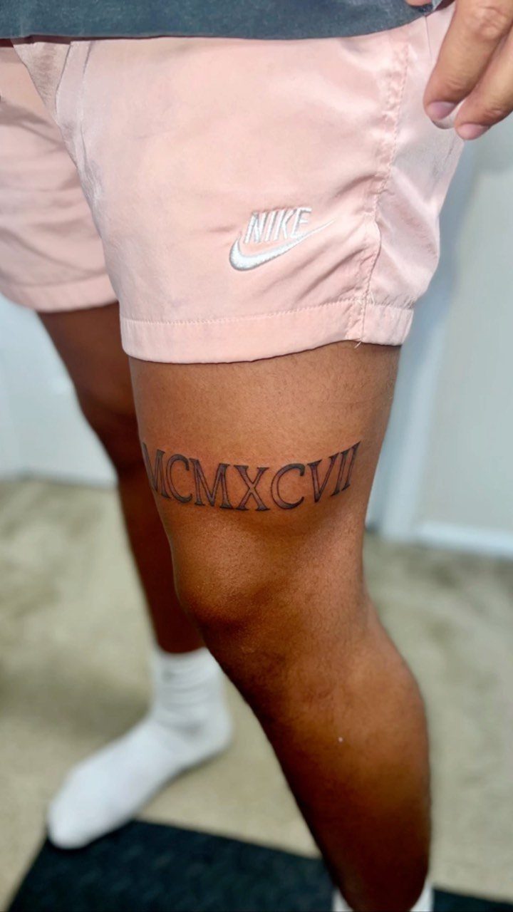 Roman numeral tattoo on a person's thigh wearing pink athletic shorts
